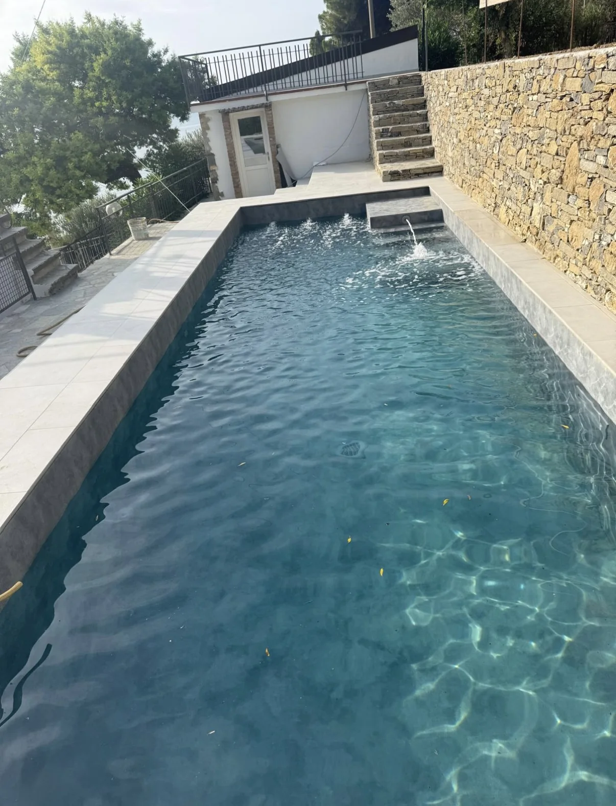 Piscina rivestita in grigio con muro di contenimento in pietra e scala